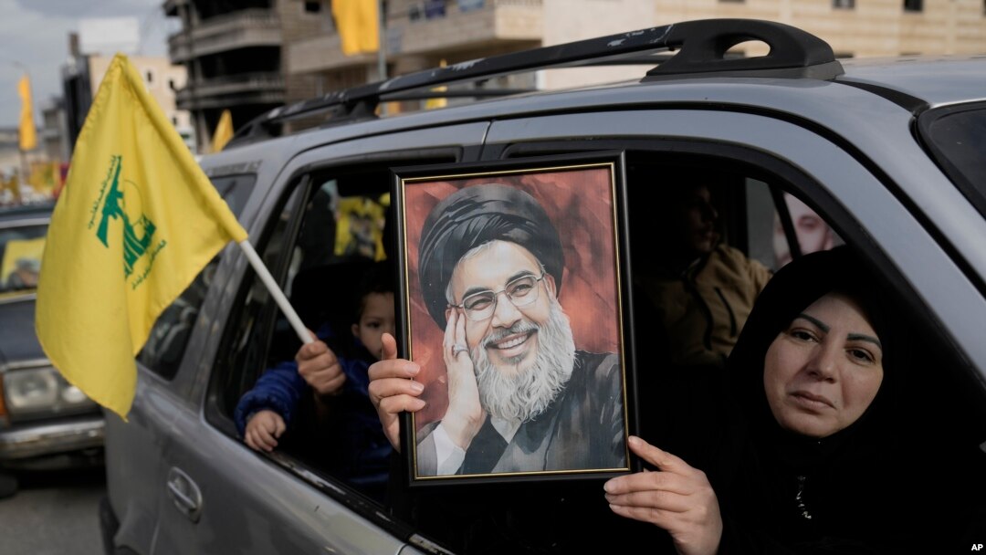 Seorang warga Lebanon memegang poster bergambar wajah Hassan Nasrallah, pemimpin Hizbullah yang tewas dibunuh, dalam perjalanannya kembali ke desa tempat tinggalnya, di Kota Bint Jbeil, di selatan Lebanon, pada 26 Januari 2025. (Foto: AP/Bilal Hussein)