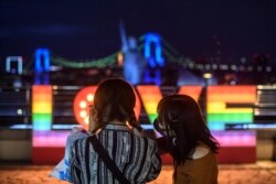 Warga mengenakan masker saat selfie di area Odaiba Tokyo pada malam hari, 12 Juli 2020. (Foto: Philip FONG / AFP)