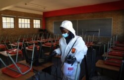 A worker from Bidvest Prestige wearing protective gear, sprays disinfectant in a classroom to help reduce the spread the new coronavirus ahead of the reopening of Landulwazi Comprehensive School, east of Johannesburg, South Africa, May 26, 2020.