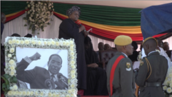 Junior Shuvai Gumbochuma, sister of Zimbabwe’s former first lady Grace Mugabe, speaks behind a photo of the late president Robert Mugabe, at his burial in Zvimba, Zimbabwe, Sept. 28, 2019. (C. Mavhunga/VOA)