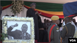 FILE: unior Shuvai Gumbochuma, sister of Zimbabwe’s former first lady Grace Mugabe, speaks behind a photo of the late president Robert Mugabe, at his burial in Zvimba, Zimbabwe, Sept. 28, 2019. (C. Mavhunga/VOA)