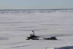 A man driving a snowmobile pulling a trailer on the frozen Bering Sea in Nome, Alaska.