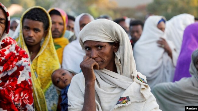 FILE - A woman stands in line with others to receive food donations at a school, which was turned into a temporary shelter for people displaced by conflict, in the town of Shire, in Ethiopia's Tigray region, March 15, 2021.