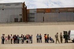 FILE - Members of the Border Patrol and U.S. military talk with migrants who illegally crossed the border between Mexico and the U.S. to request political asylum, as seen from Ciudad Juarez, Mexico, July 6, 2019.