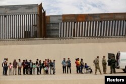 FILE - Members of the Border Patrol and U.S. military talk with migrants who illegally crossed the border between Mexico and the U.S. to request political asylum, as seen from Ciudad Juarez, Mexico, July 6, 2019.