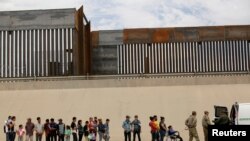 FILE - Members of the Border Patrol and U.S. military talk with migrants who illegally crossed the border between Mexico and the U.S. to request political asylum, as seen from Ciudad Juarez, Mexico, July 6, 2019. 