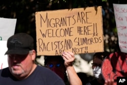 A protester holds up a placard during a rally staged by the East Colfax Community Collective to address chronic problems in the apartment buildings occupied by people displaced from Central and South America, on Sept. 3, 2024, in Aurora, Colorado.