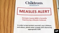 In this May 2, 2017, photo, a sign at a clinic in Minneapolis, alerts patients to a measles outbreak in the area. The sign is posted in multiple languages outside the clinic's lobby to let parents know about precautions the hospital is taking to try to keep the disease from spreading.