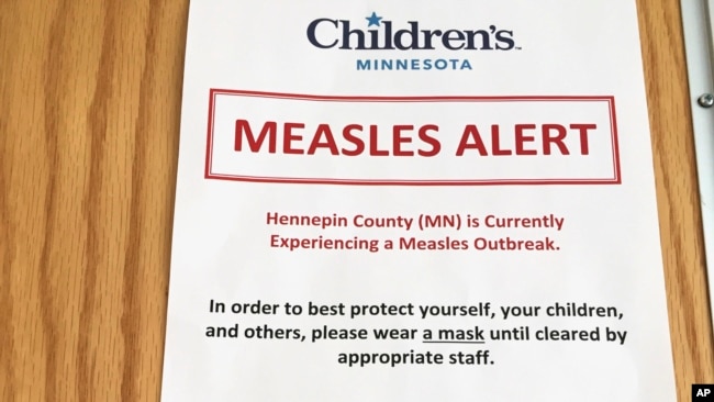 In this May 2, 2017, photo, a sign at a clinic in Minneapolis, alerts patients to a measles outbreak in the area. The sign is posted in multiple languages outside the clinic's lobby to let parents know about precautions the hospital is taking to try to keep the disease from spreading.