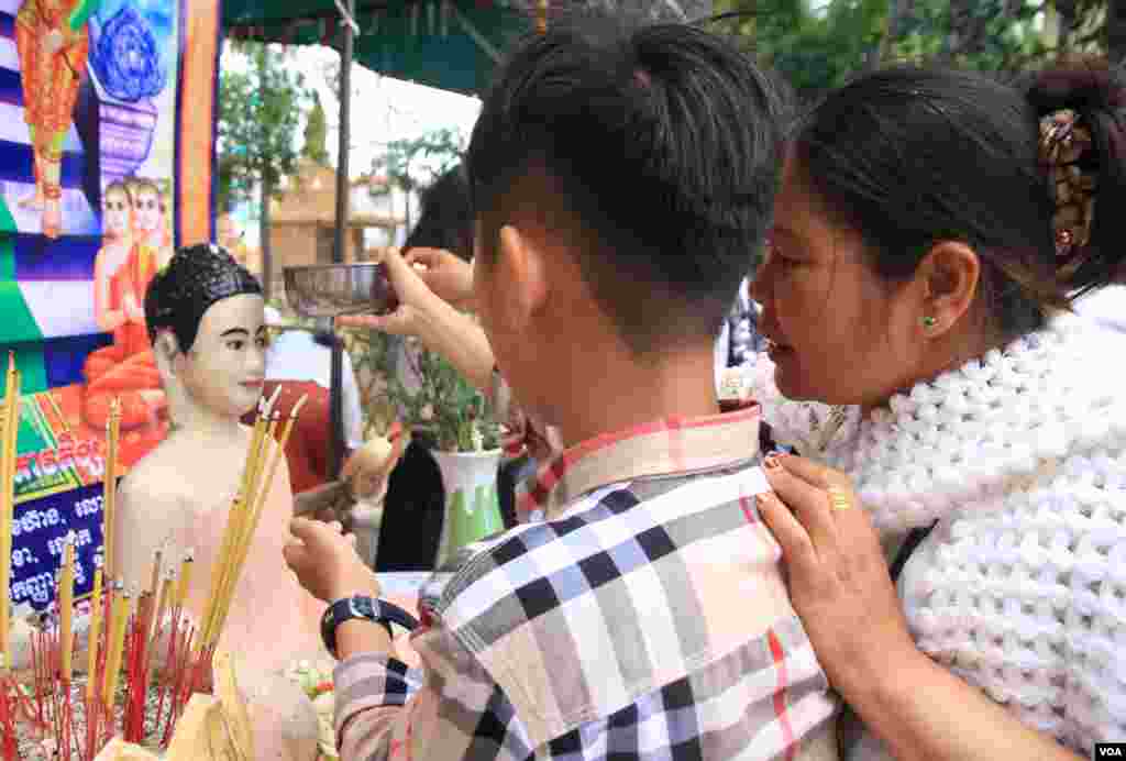 ប្រជាពលរដ្ឋខ្មែរ បង្រៀនកូនខ្លួនឲ្យចេះស្រង់ព្រះ នៅថ្ងៃបុណ្យចូលឆ្នាំខ្មែរ ក្នុងវត្តមួយជាយរាជធានីភ្នំពេញ កាលពីថ្ងៃទី១៤ ខែមេសា ឆ្នាំ២០១៧។ (ហ៊ាន សុជាតា/VOA)