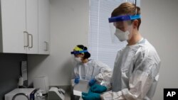 FILE - Wayne State University medical school students Lucia Luna-Wong, left and Michael Moentmann work in a COVID-19 testing center in Detroit, April 24, 2020. 