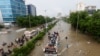 FILE - People sit atop a bus roof while others wade through the flooded road during monsoon rain, in Karachi, Pakistan Aug. 27, 2020. 