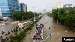 FILE - People sit atop a bus roof while others wade through the flooded road during monsoon rain, in Karachi, Pakistan Aug. 27, 2020. 