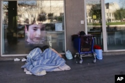 A homeless sleeps under blankets in front of the entrance of a bank, in Milan, Italy, Jan. 7, 2017. In Italy, sub-freezing temperatures were blamed on the deaths of a half-dozen homeless people, while heavy snows and high winds resulted in re-routed fligh