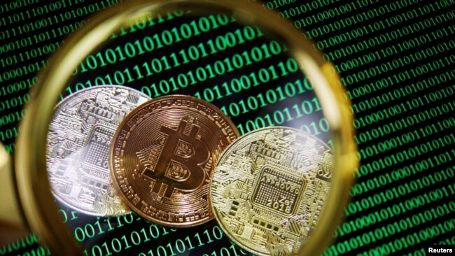 Representations of Bitcoin and other cryptocurrencies on a screen showing binary codes are seen through a magnifying glass in this illustration picture taken Sept. 27, 2021.