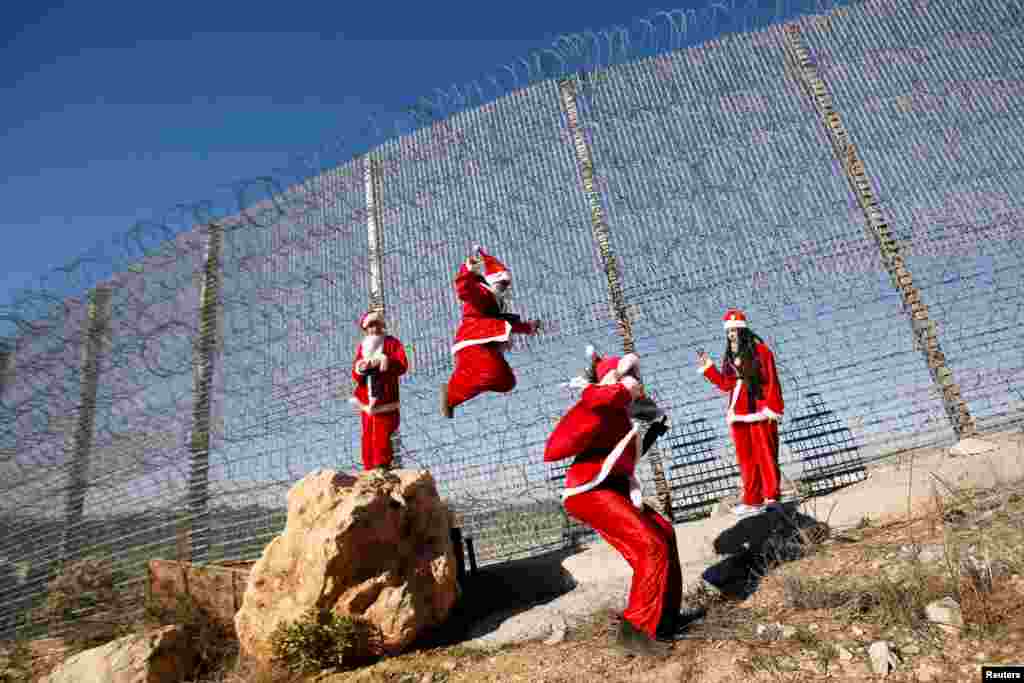 Palestinian children dressed as Santa Claus jump near the Israeli barrier during an anti-Israel protest, near Bethlehem in the Israeli-occupied West Bank, Dec. 23, 2019.