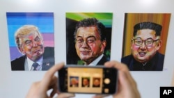 A visitor takes a photograph of images, from left, of U.S. President Donald Trump, South Korean President Moon Jae-in and North Korean leader Kim Jong Un during an exhibition at an annex of the presidential Blue House in Seoul, South Korea, Jan. 3, 2019. 