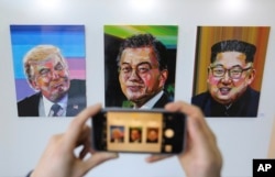 A visitor takes images, from left, of U.S. President Donald Trump, South Korean President Moon Jae-in and North Korean leader Kim Jong Un during an exhibition at an annex of the presidential Blue House in Seoul, South Korea, Jan. 3, 2019.