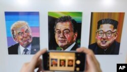 A visitor takes images, from left, of U.S. President Donald Trump, South Korean President Moon Jae-in and North Korean leader Kim Jong Un during an exhibition at an annex of the presidential Blue House in Seoul, South Korea, Jan. 3, 2019. 