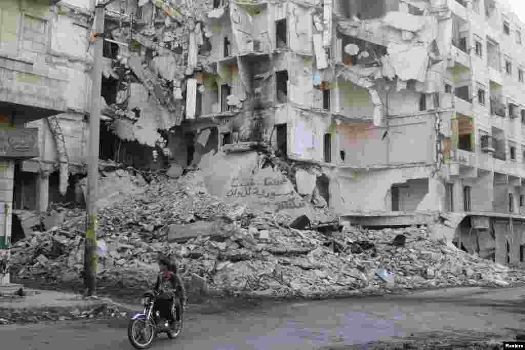 Dua pria mengendarai sepeda motor melewati gedung-gedung yang hancur di distrik Bustan al-Basha, kota Aleppo, Suriah.&nbsp;