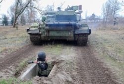 FILE - A reservist of the Ukrainian Territorial Defense Forces throws a dummy grenade towards an armored vehicle during military exercises at a training ground outside Kharkiv, Ukraine Dec. 11, 2021.