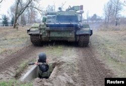 FILE - A reservist of the Ukrainian Territorial Defense Forces throws a dummy grenade towards an armored vehicle during military exercises at a training ground outside Kharkiv, Ukraine Dec. 11, 2021.