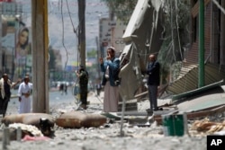 FILE - A man uses his cell phone to take pictures of houses destroyed by a Saudi-led airstrike in Sana'a, Yemen, June 8, 2015.