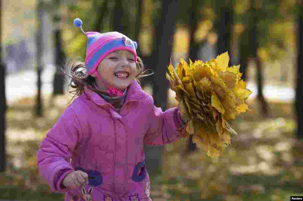 A girl runs with autumn leaves she gathered at a park in Donetsk, eastern Ukraine. 