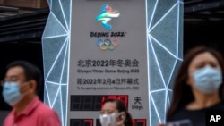 2021nian 8月18日，几名带口罩的民众走过一个2022年北京冬奥会倒计时看板。 
