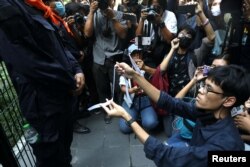 A protester makes a white ribbon as a symbol of peace in front of a police officer during anti-government protests in Bangkok, Thailand October 15, 2020. (REUTERS/Soe Zeya Tun)