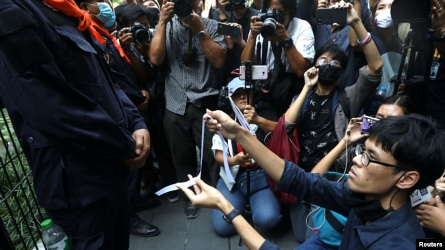 A protester makes a white ribbon as a symbol of peace in front of a police officer during anti-government protests in Bangkok, Thailand October 15, 2020. REUTERS/Soe Zeya Tun