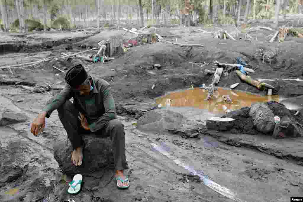 A man rests on a rock while visiting the area that he believes his grandchild is buried following the Mount Semeru volcano eruption in Sumberwuluh, Indonesia.