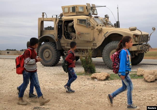 FILE - Syrian schoolchildren walk as U.S. troops patrol near the Turkish border in Hasakah, Syria, Nov. 4, 2018.