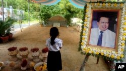 FILE - A girl stands by a portrait of Kem Ley, a Cambodian prominent political analyst, at his grave in Ang Takok, Cambodia, Nov. 20, 2016.