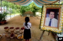 FILE - A girl stands by a portrait of Kem Ley, a Cambodian prominent political analyst, at his grave in Ang Takok, Cambodia, Nov. 20, 2016.