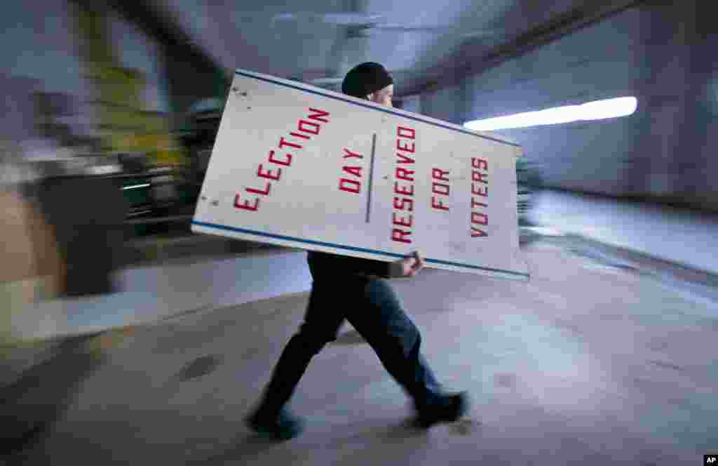 Firefighter Cheyne Hansen takes a sign out of storage at a municipal garage while helping election officials scramble to set up a last-minute polling place, Nov. 4, 2014, in Camden, Maine. 