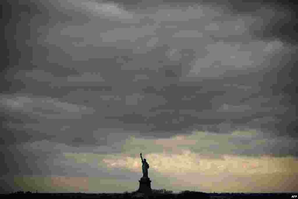 Cloudy skies hang over the The Statue of Liberty as seem from the Staten Island Ferry near New York City, US.