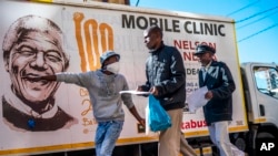 FILE - A volunteer directs two men towards a medical tent where they will be tested for COVID-19 as well as HIV and Tuberculosis, in downtown Johannesburg Thursday, April 30, 2020. 