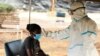 FILE - A woman has her temperature checked by a health care worker during a nationwide lockdown to help curb the spread of the coronavirus, at a screening center in Harare, Zimbabwe, April 30, 2020.