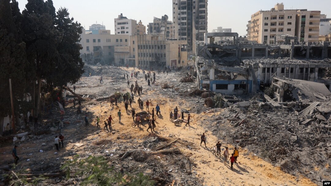 Orang-orang berjalan di atas puing-puing di kompleks gedung Badan Bantuan PBB untuk Pengungsi Palestina (UNRWA) yang rusak di lingkungan Al-Sinaa, Jalur Gaza barat hari Jumat 12 Juli 2024, pasca penarikan pasukan Israel dari daerah tersebut.