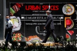 Personas con mascarillas pasan junto a un cartel que anuncia un restaurante en la Ciudad de México, el viernes 5 de junio de 2020.