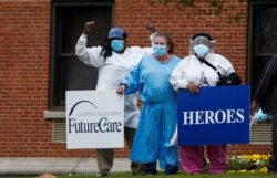 FILE - Medical workers pose for photos taken by coworkers as they stand with signs saying "Heroes Work Here" that have been placed outside the FutureCare Lochearn senior nursing facility, Baltimore, Maryland, April 17, 2020.