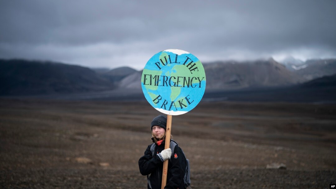 Seorang gadis memegang papan bertuliskan 'pull the emergency brake' ketika ia menghadiri upacara di daerah yang dulunya adalah gletser Okjokull, di Islandia, Minggu, 18 Agustus 2019. (Foto: AP)