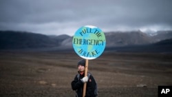 Seorang gadis memegang papan bertuliskan 'pull the emergency brake' ketika ia menghadiri upacara di daerah yang dulunya adalah gletser Okjokull, di Islandia, Minggu, 18 Agustus 2019. (Foto: AP)