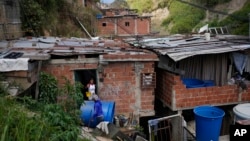 FILE - Franklin Caceres talks with Banesky Fuentes as he fills her container with water pumped from a well in Caracas, Venezuela, March 20, 2023. In the crisis-ridden country, water, electricity and other public services are unreliable, and food prices have skyrocketed.