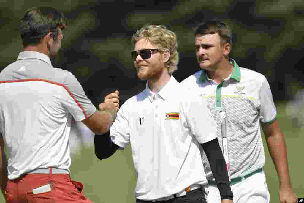 Scott Vincent of Zimbabwe bumps fist with Corey Conners of Canada as Christiaan Bezuidenhout of South Africa looks on. REUTERS/Toby Melville