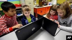 FILE - Second-grader Josh Mercado, left, helps kindergartner Erik Hodges, as second-grader Annabelle Davis, right, helps kindergartner Kaidyance Harris, on programming during their weekly computer science lesson at Marshall Elementary School in Marysville