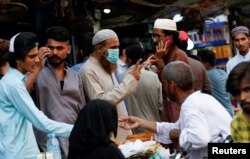 FILE - A man wearing a protective face mask gestures while shopping outside an electronics market, after Pakistan started easing lockdown restrictions, as the outbreak of the coronavirus disease continues, in Karachi, Pakistan, June 4, 2020.