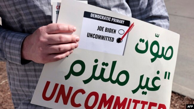 A volunteer holds a sign asking people to vote uncommitted, instead of for US President Joe Biden, outside of Maples School in Dearborn, Michigan, on Feb. 27, 2024.
