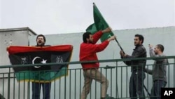 Libyans who live in Greece remove the Libyan flag from a Libyan state school as another shouts slogans and holds the old flag of his country during a protest in Athens, Tuesday, Feb. 22, 2011. About 60 Libyans gathered at the protest against Gadhafi's cra